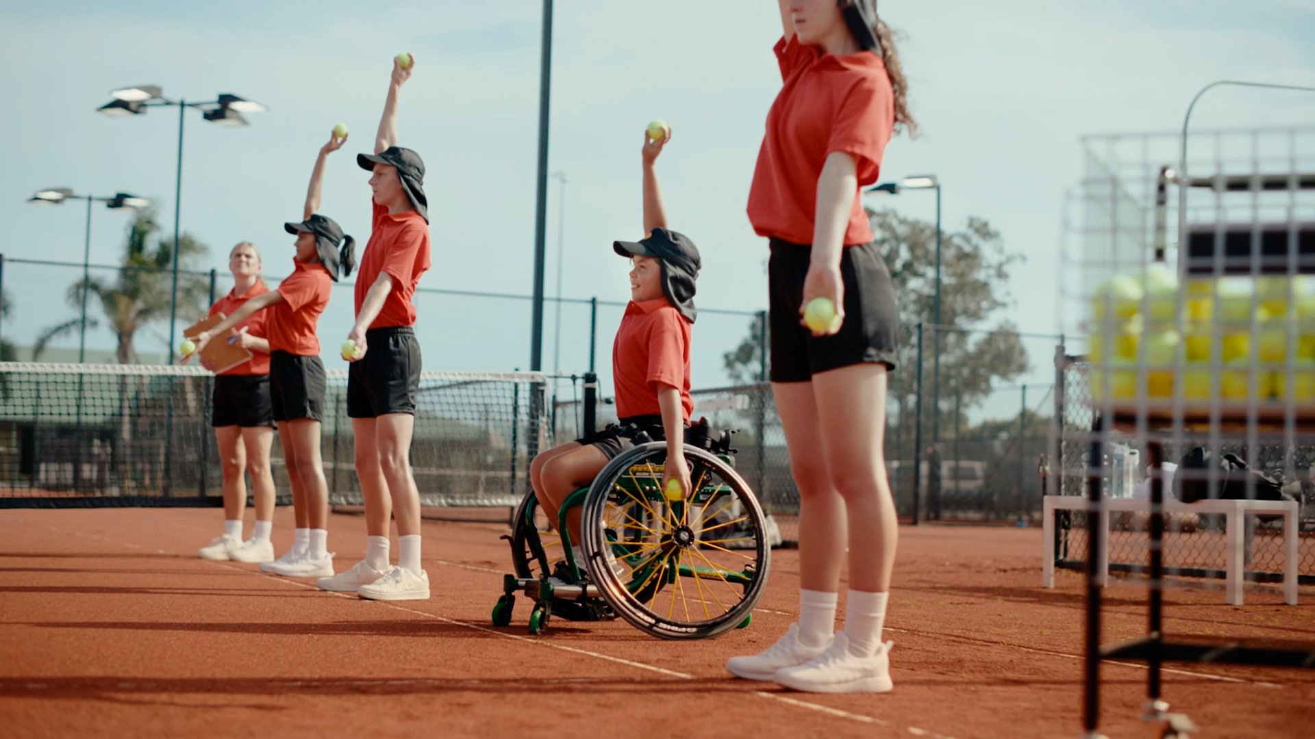 Kids including wheelchair athlete in line on tennis court